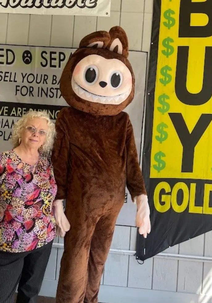 Denise with the LBC mascot in front of the We Buy Gold banner